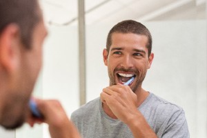 Man smiling while brushing his teeth in bathroom